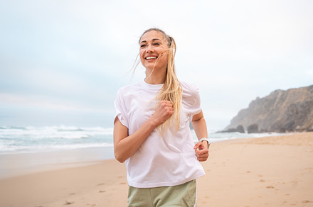 Smiling young woman runner jogging on sandy beach near sea, a Person Photo by andreonegin market