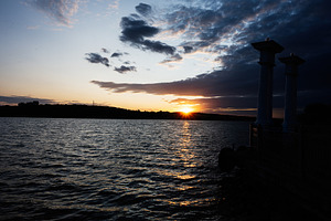 Scenic evening sunset view over a calm lake with silhouetted columns, a Photo by AS photostudio