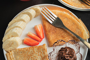 A plate of crepes filled with chocolate spread and topped with banana slices an, a Food & Drink Photo by Budarinphoto