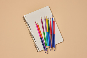 Top view of an open notebook with pastel-colored pencils on a be, a School & Education Photo by ndanko