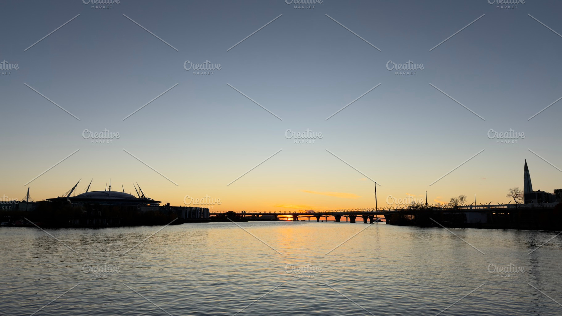A serene sunset over a river, with silhouettes of buildings and a bridge in the, a Nature Photo by Textures & Backgrounds