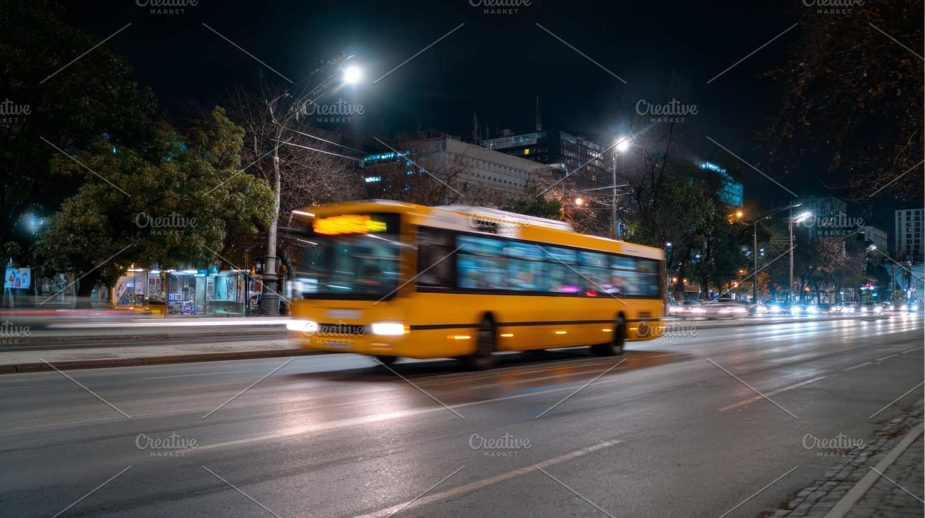A vibrant yellow bus speeds through a city street at night, illuminated by stre, a Business Photo by ImageMir