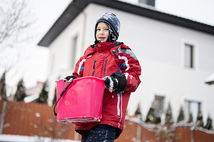 Boy hold bucket with snow against house in winter. Active outdoo, a Person Photo by AS photostudio