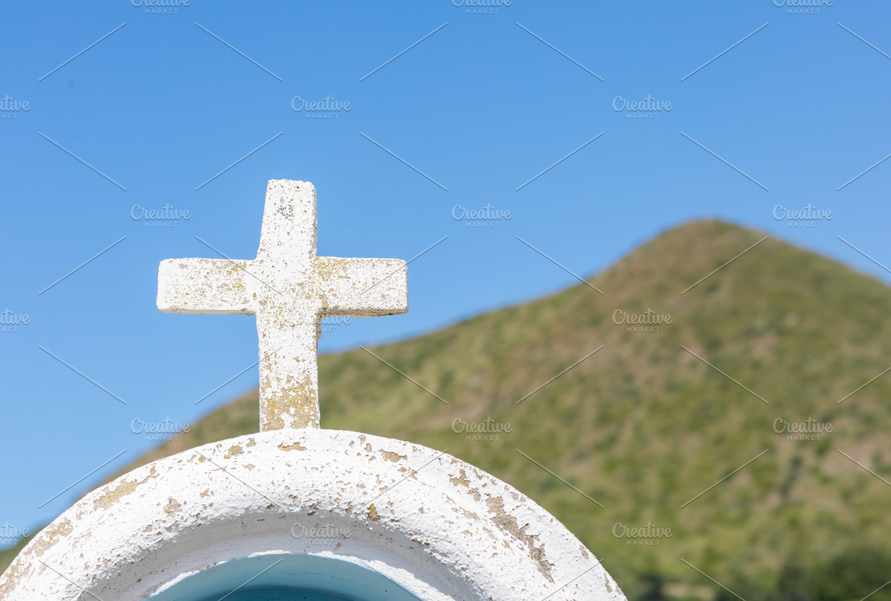 White cross overlooking a green hill under a clear blue sky, a Photo by Antonio Gravante Market