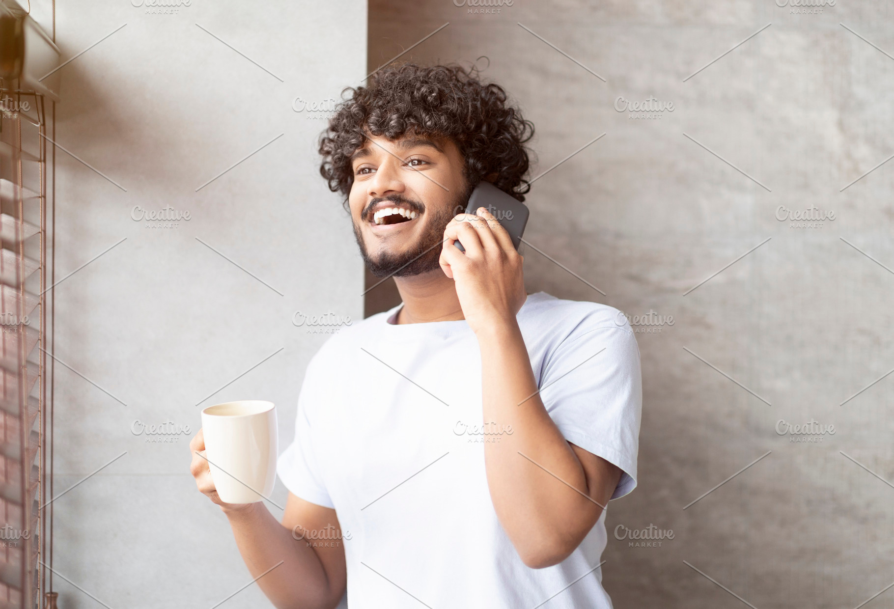 Happy indian man having phone conversation, standing in bathroom with cup in ha, a Person Photo by Prostock-Studio