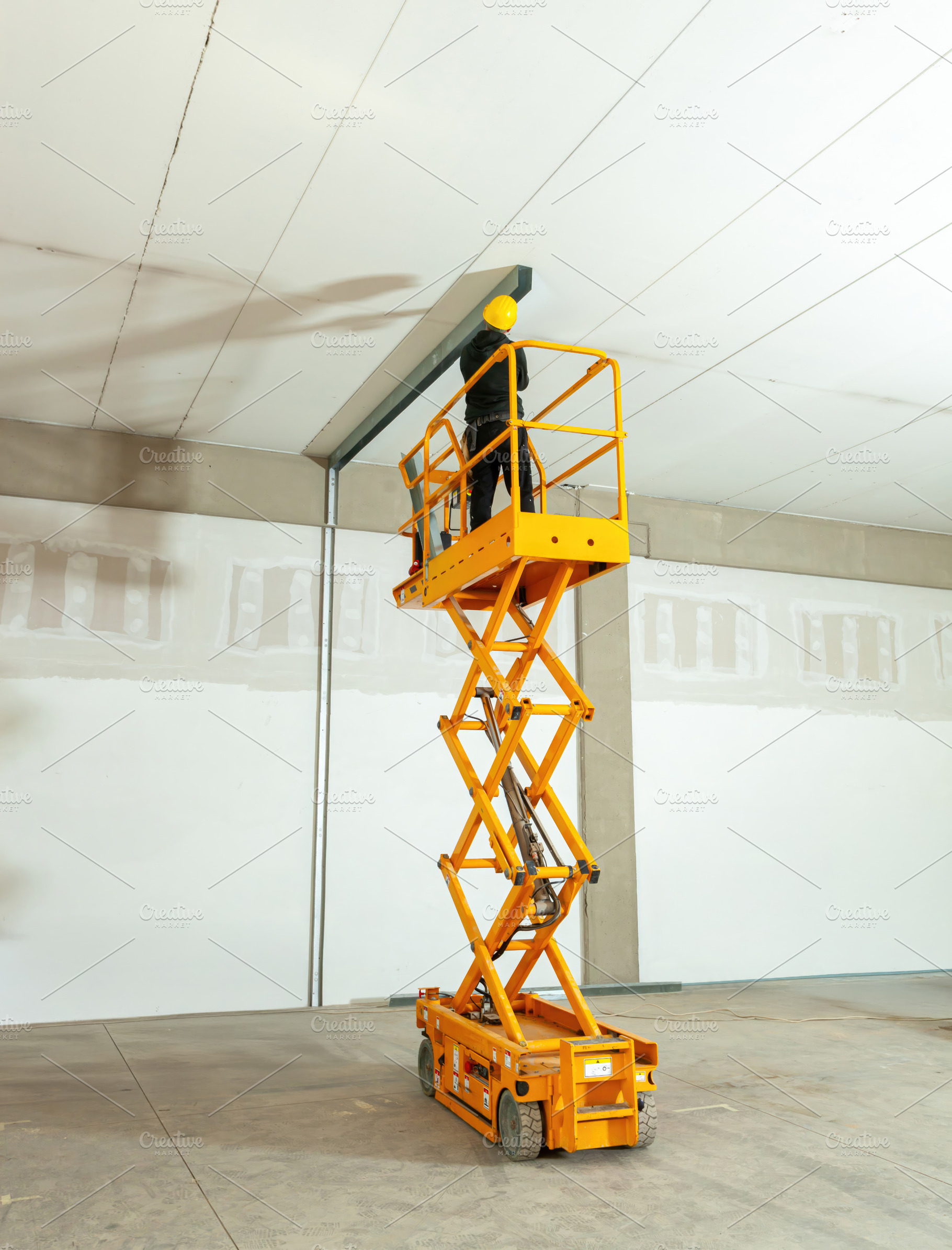 Construction worker using scissor lift to install ceiling beams in warehouse, an Industrial Photo by Antonio Gravante Market