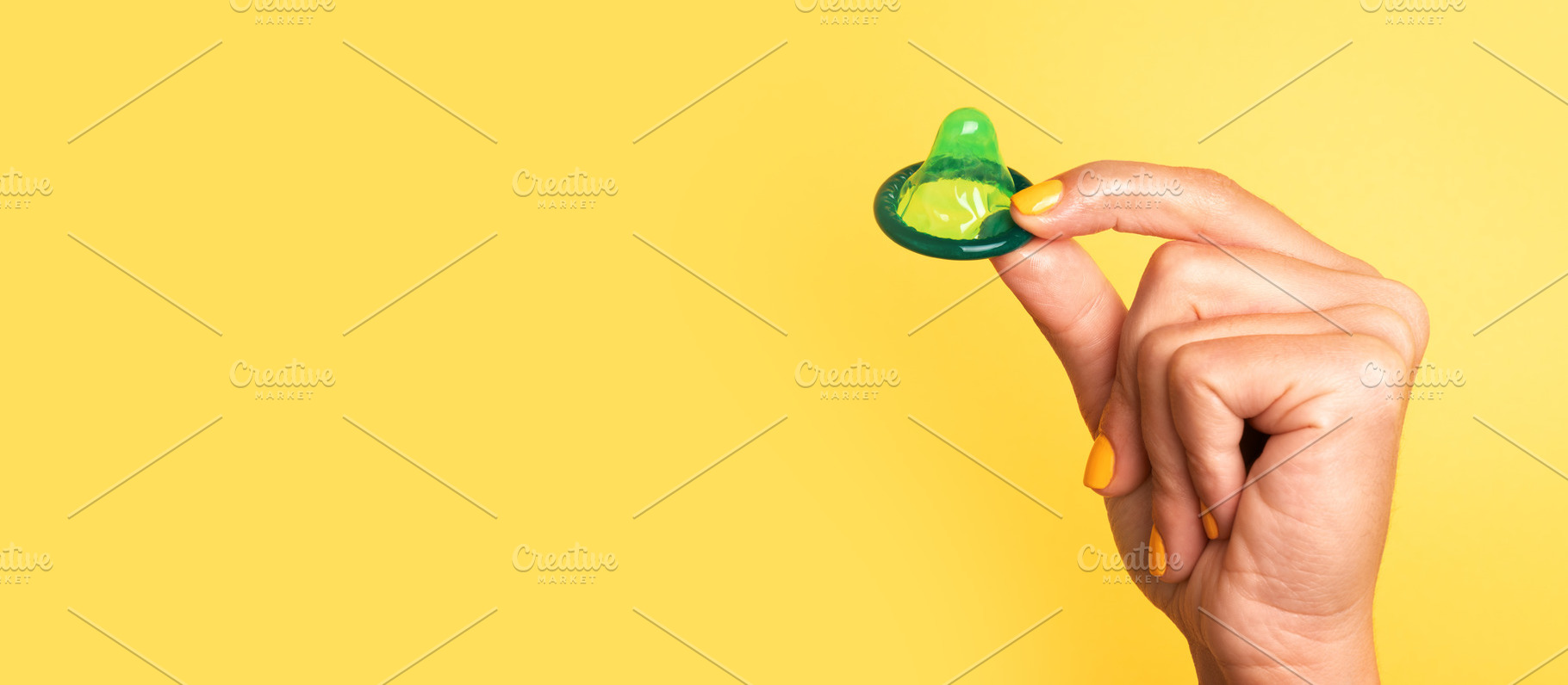 Hand with yellow-painted nails holding a green lubricated condom, a Health & Medical Photo by Ales Munt