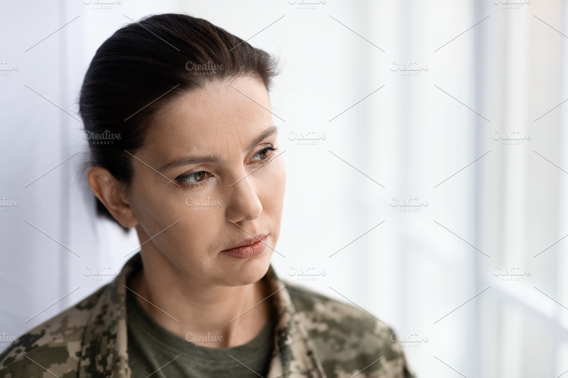 Thoughtful female soldier wearing camouflage uniform looking through window at, a Photo by Prostock-Studio
