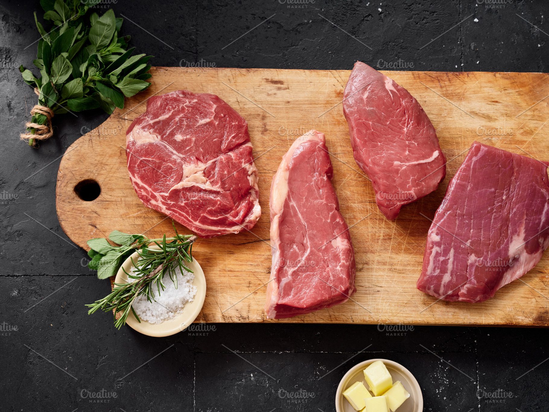 Different cuts of raw beef on a wooden cutting board with herbs and butter in a, a Food & Drink Photo by Asya Nurullina