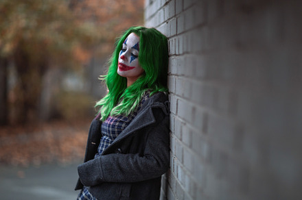Portrait of a greenhaired girl in chekered dress with joker makeup on a brick w