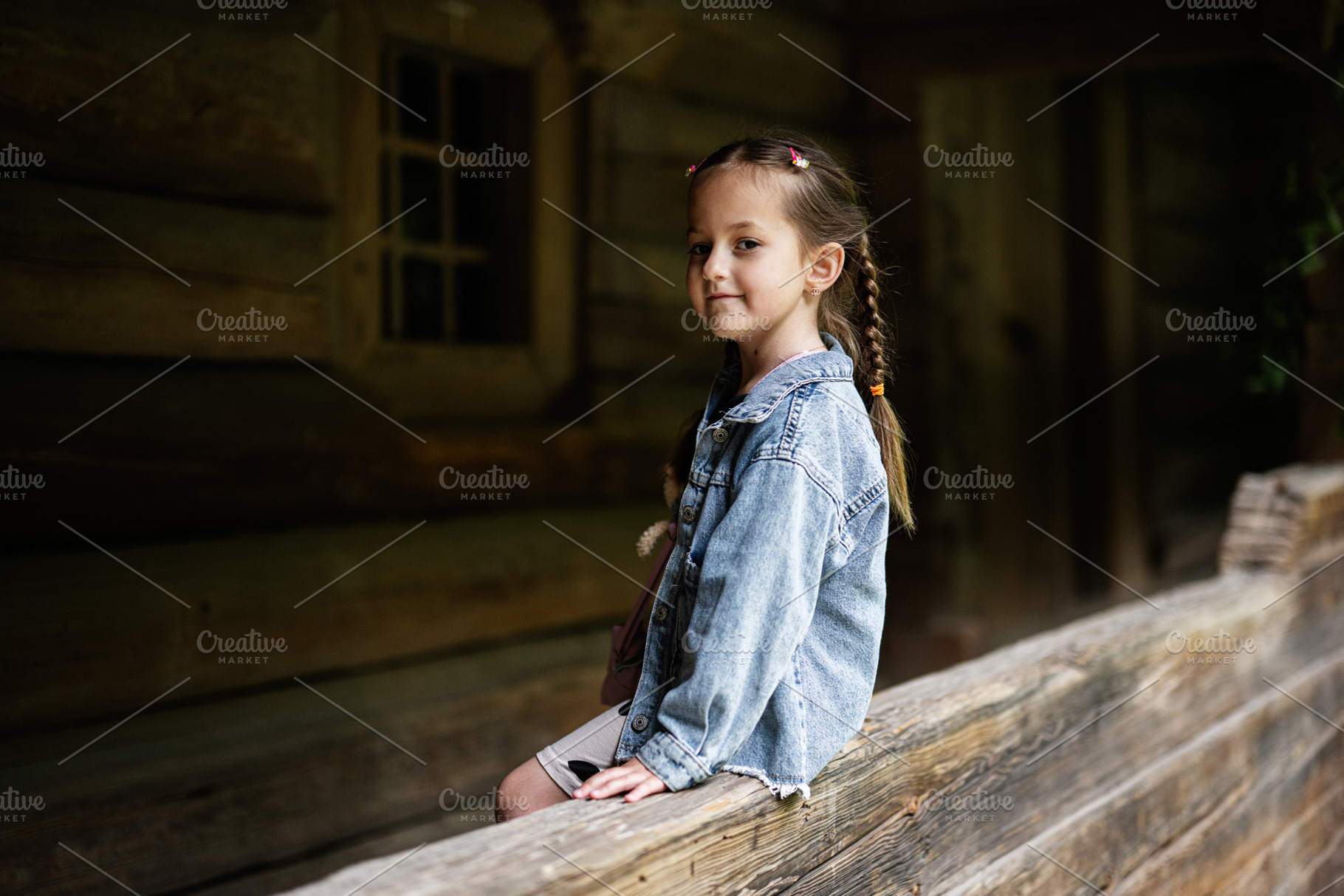 Young girl sitting outdoors by a wooden cabin with a gentle smile, a Person Photo by AS photostudio