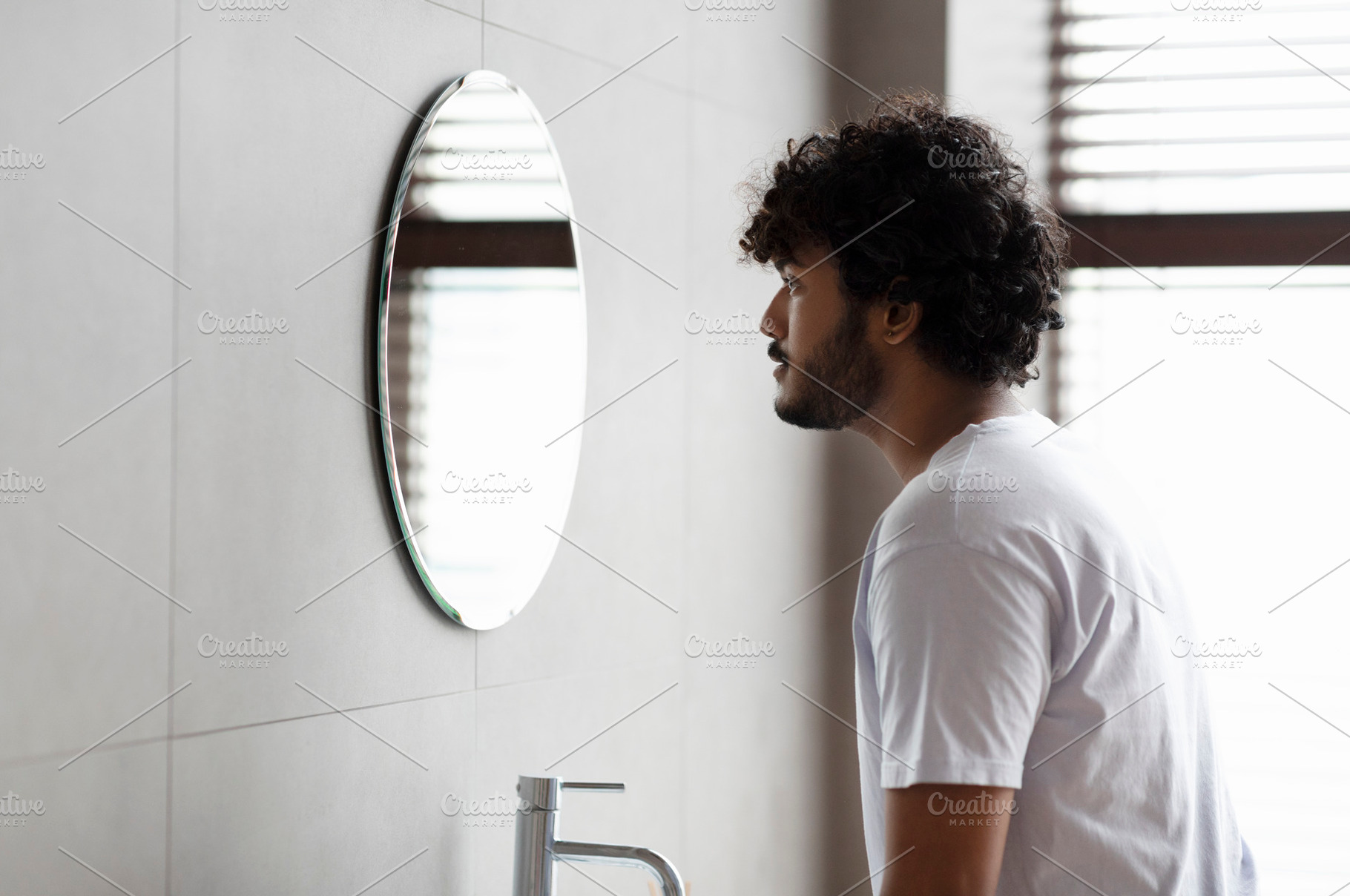 Male beauty. Young indian man standing in bathroom and looking in mirror at his, a Person Photo by Prostock-Studio