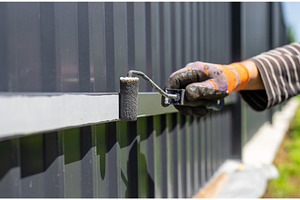 Man painting a metal fence, an Industrial Photo by yanadjana