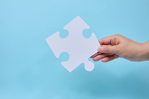 A person holding a single white puzzle piece against a blue back, a Business Photo by ndanko