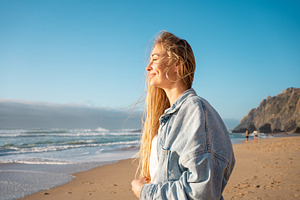 Smiling thoughtful woman on seashore against blue sky at beach, a Photo by andreonegin market