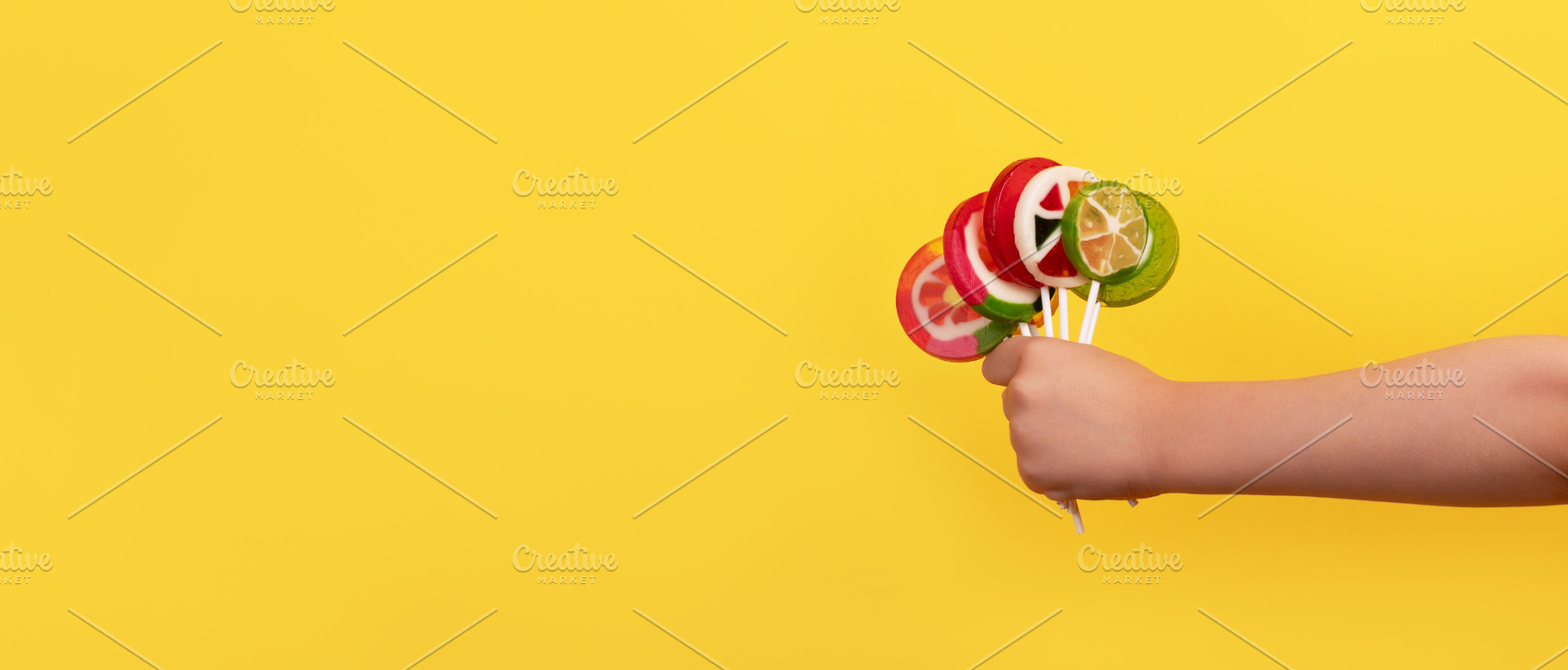 Kid's hand holding a bunch of vibrant fruit-shaped lollipops on, a Food & Drink Photo by Ales Munt
