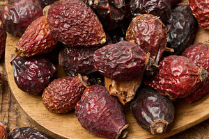 Dried rosehip fruits in a wooden spoon and on a table close-up., a Food & Drink Photo by ndanko
