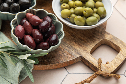 Green, black and kalamata olives in bowls on wooden board, a Food & Drink Photo by Olena Rudo