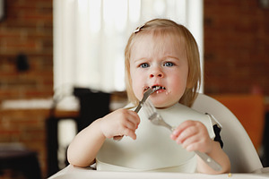 Infant girl or toddler sitting on high chair. Eating food by herself using spoo, a Person Photo by Lenor4ik