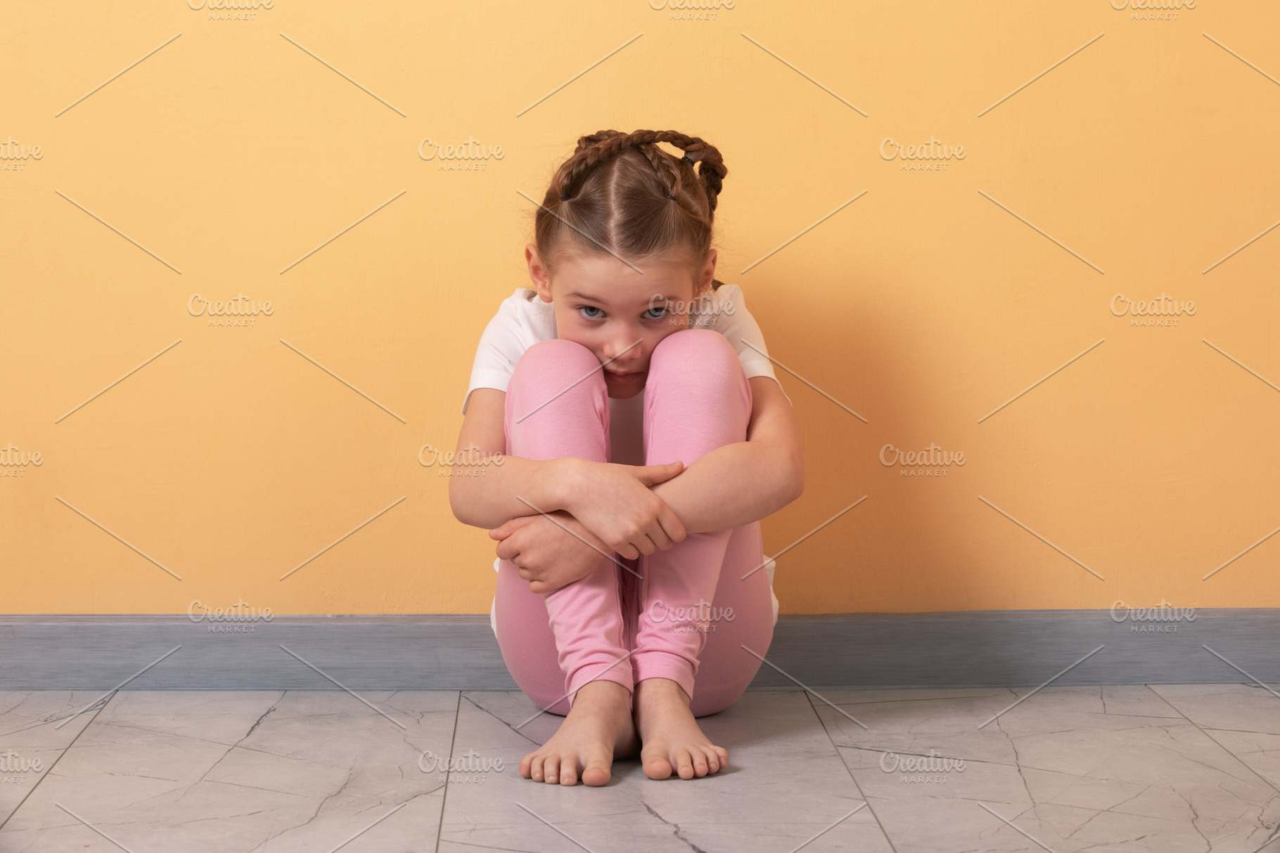 Young girl in pink leggings sits on floor against yellow wall, h, a Person Photo by Ales Munt