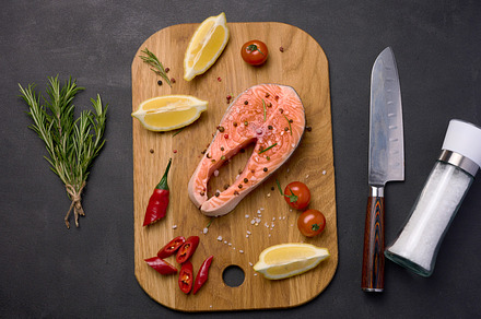 Raw salmon steak on a wooden cutting board, lemon slices, spices, a Food & Drink Photo by ndanko