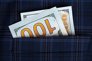 Close-up of two US hundred dollar bills sticking out of a blue plaid fabric poc, a Business Photo by Ales Munt