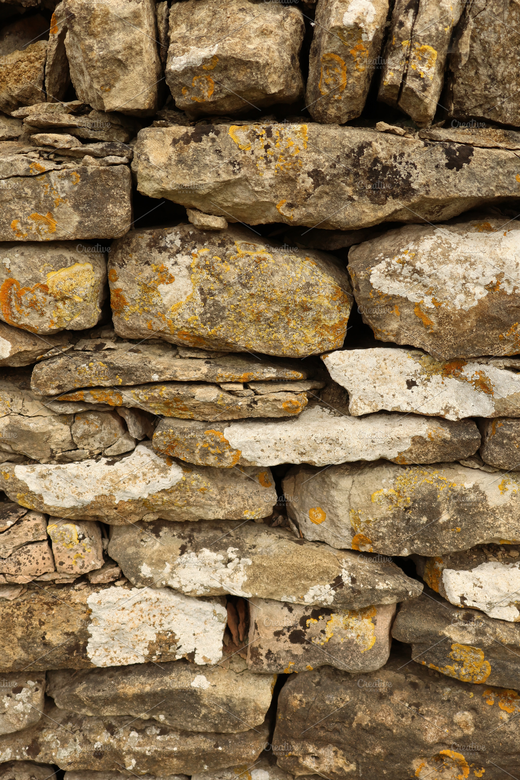 Dry stone wall texture with weathered stones and colorful lichen, natural rusti, a Photo by Studio ANNA