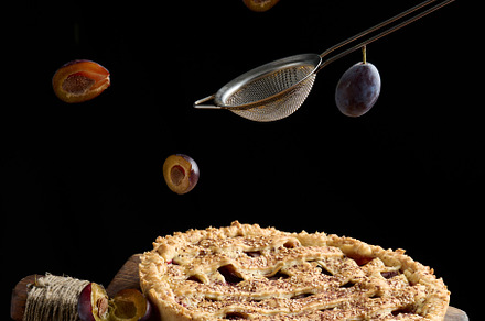 baked round pie with plums on a levitating wooden kitchen board,, a Photo by ndanko