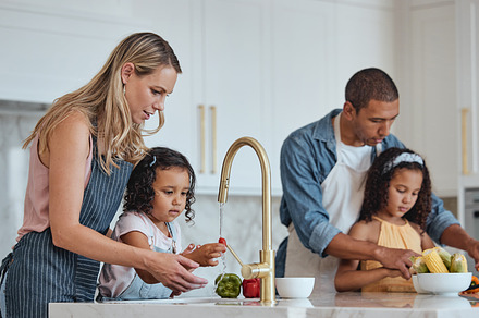 Family, mother and father with girls in kitchen, rinse vegetables and bonding. Love, mama and dad with daughters, child development or loving to prepare salad together for lunch, veggies or childcare, a Photo by Peopleimages.com