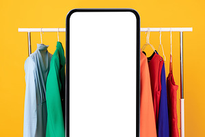 Big Smartphone Blank Screen Standing Near Clothing Rail, Yellow Background, a Photo by Prostock-Studio