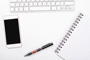 Top view of smartphone and computer keyboard next to notebook and pen on
