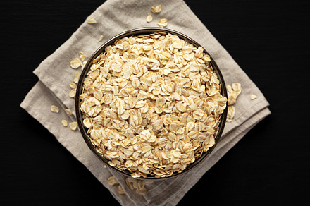 Wholegrain Oat Flakes in a Bowl on a black background, top view., a Food & Drink Photo by LiudmylaChuhunova