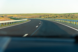 Smooth asphalt highway curving through open countryside with guardrails, clear, a Transportation Photo by Ales Munt