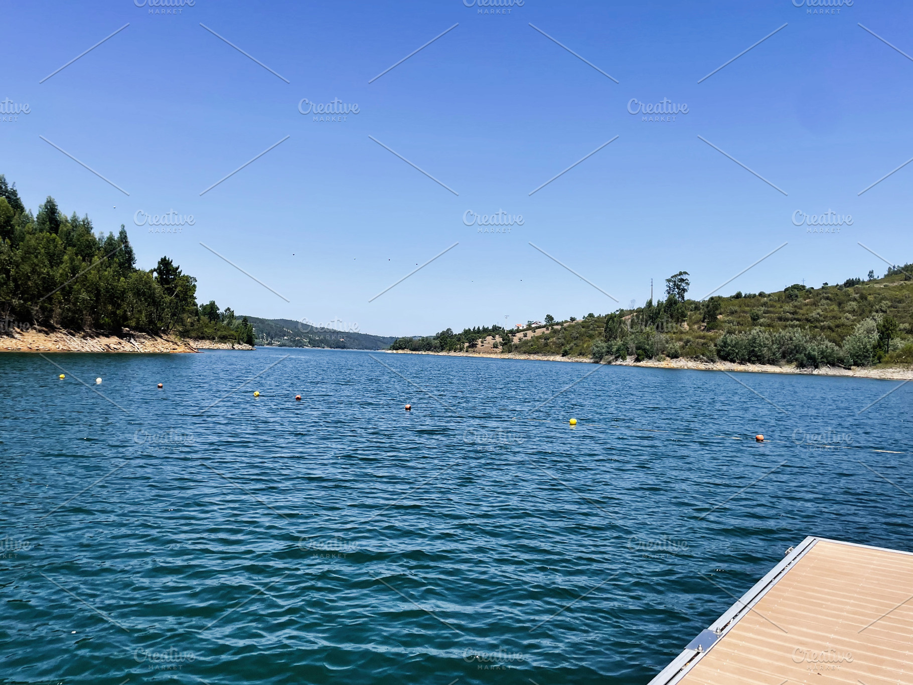 Scenic lake view with hills and dock in central Portugal under clear blue skies, a Photo by AS photostudio