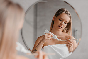 Young lady cleaning teeth in the morning, applying toothpaste on toothbrush, st, a Photo by Prostock-Studio
