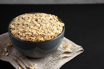 Wholegrain Oat Flakes in a Bowl on a black background, side view, a Food & Drink Photo by LiudmylaChuhunova