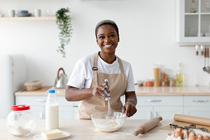 Smiling pretty millennial african american woman chef in apron making dough in, a Person Photo by Prostock-Studio