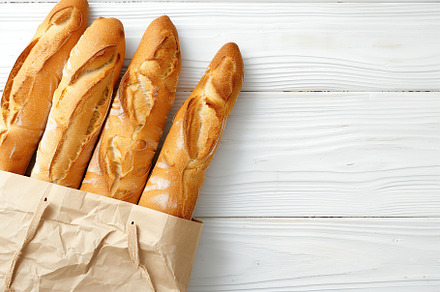 Freshly baked baguette in paper bag on wooden table, a Food & Drink Photo by AlyaAnd