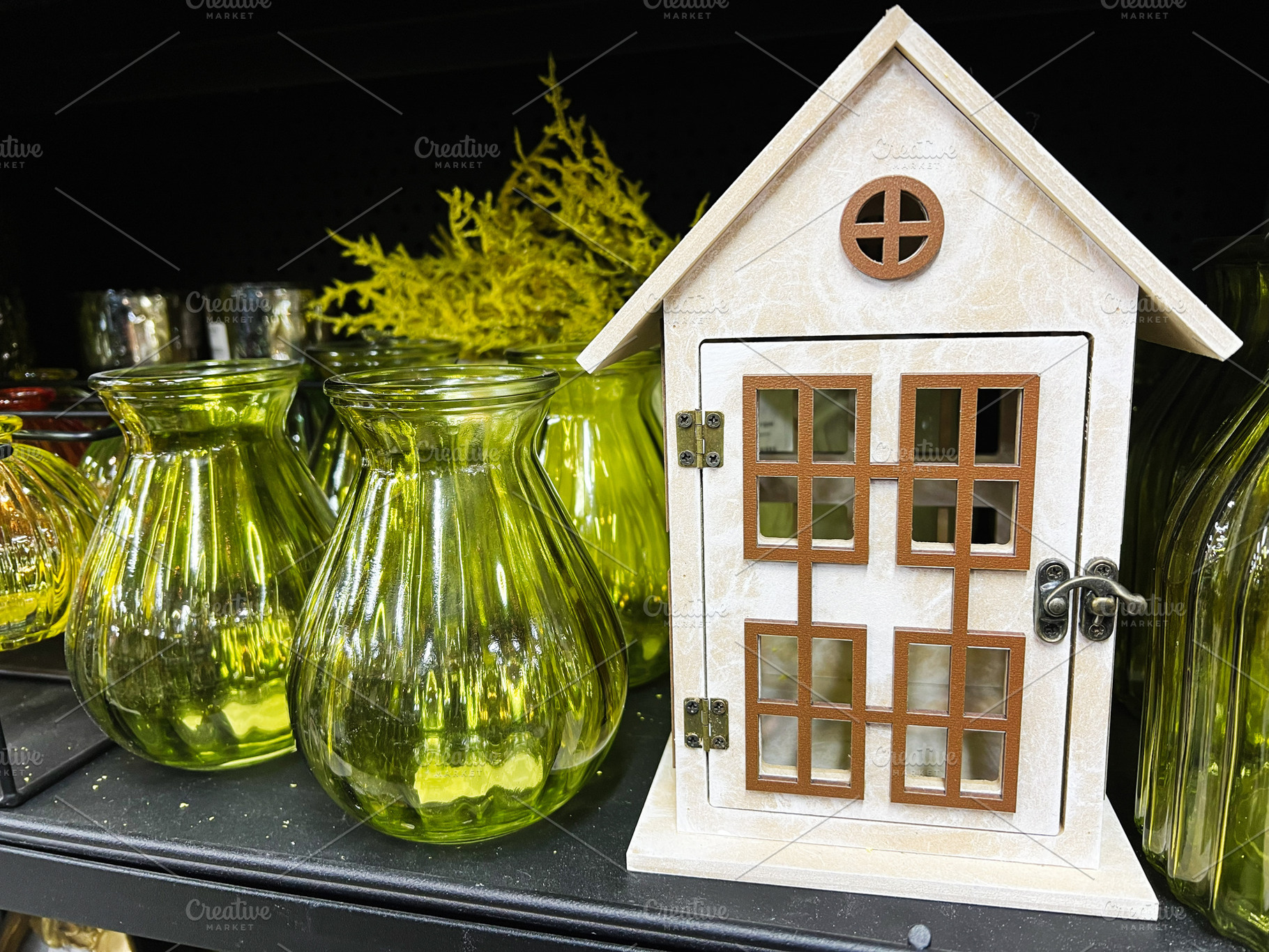 Decorative miniature house with green glass vases on a black shelf, a Photo by AS photostudio