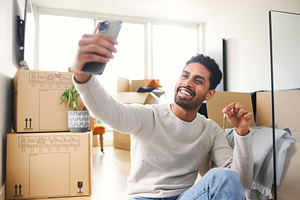 Man With Mobile Phone Moving Into New Home Making Video Call Holding Keys Surro