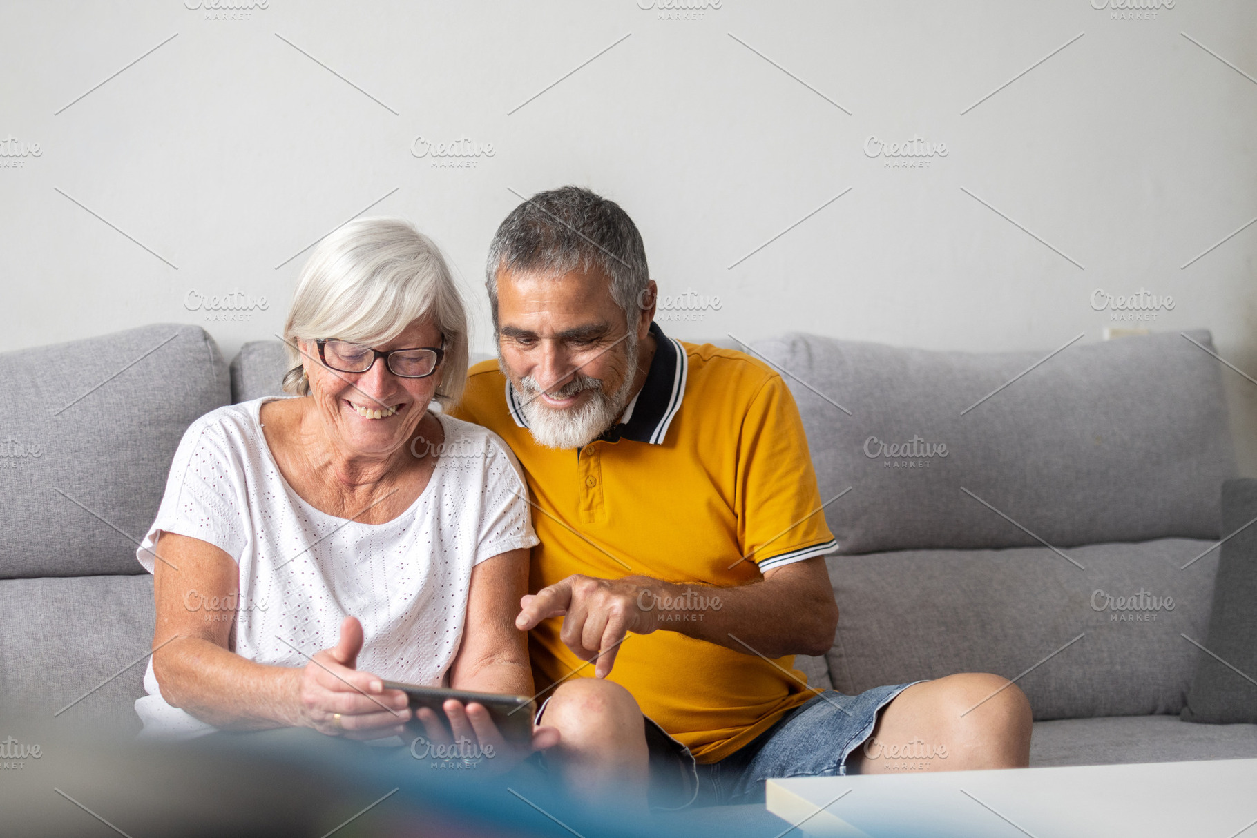 Senior couple using smartphone together on sofa at home, a Person Photo by etorres69