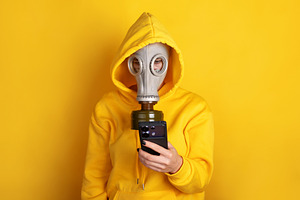 Individual in yellow hoodie and gas mask holding smartphone agai, a Person Photo by Ales Munt