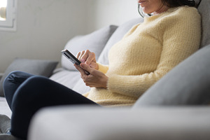 Woman using smartphone while relaxing on sofa at home in natural light, a Person Photo by etorres69