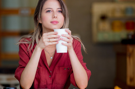 young woman in a red dress with a cup of coffee sits at a table, a Person Photo by Masson Simon
