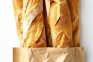 Freshly baked baguette in paper bag isolated on white background, a Food & Drink Photo by AlyaAnd