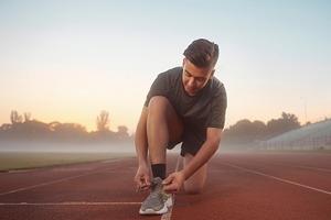 Runner tying shoe on track at foggy morning, a Photo by DanFLCreativo