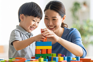 Child building with blocks under supervision of a smiling adult, a School & Education Photo by DanFLCreativo
