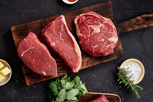 Raw rib-eye, roast beef, flank and rump steak placed on a wooden cutting board
