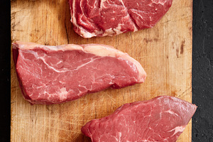 Raw beef cuts including rib-eye, roast beef, flank, and rump steak on wooden ch
