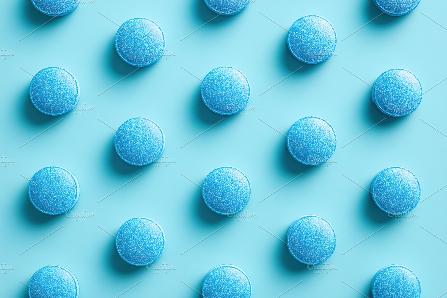 Neatly arranged blue macarons on a vibrant teal backdrop in a top-down view, a Photo by AlyaAnd